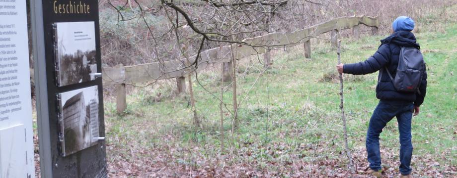 Urlaubsregion Höhbeck Elbe - Titelbild: Wanderer mit Wanderstab auf der Wiese an der ehemaligen Thalmühle, links im Bild befinden sich Tafeln des Entdeckerpfades, auf dem Boden liegt Herbstlaub.